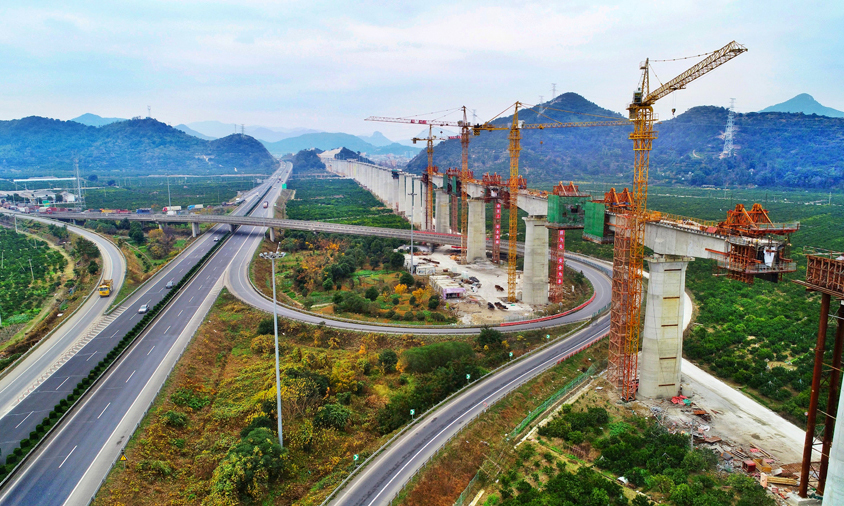 靈江特大橋上跨靈江航道、馬上線公路、S327省道、臺金高速公路，施工環(huán)境異常復(fù)雜，是全線關(guān)鍵性重難點控制工程。該橋在施工中不但要保證靈江及相鄰公路的正常通航通行、還面臨著深水基礎(chǔ)施工、大跨度連續(xù)梁施工線形監(jiān)控等一系列施工難題。特別是位于靈江中的61-67號墩，鉆孔深度達(dá)95.945米。當(dāng)鉆孔深度超過80米后，尤其在軟硬交互地層，控制樁孔的豎直度就成為一項重要的技術(shù)難題。由于樁孔直徑大、深，且存在較厚卵石層，非常容易造成護(hù)壁泥漿失效、孔壁局部或整體坍塌。因此，靈江特大橋施工也被稱為“在刀刃上跳舞”。圖為靈江特大橋連續(xù)梁合龍施工。