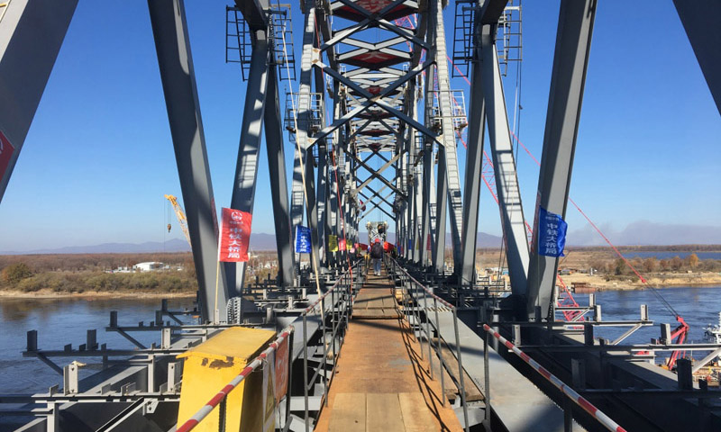 同江中俄鐵路大橋工程于2014年2月26日奠基，是中俄首座跨界河鐵路大橋，設(shè)計(jì)鐵路年過貨能力2100萬(wàn)噸。大橋全長(zhǎng)7193.71米，其中跨江大橋主橋全長(zhǎng)2215.02米，中方境內(nèi)1886.45米，俄方境內(nèi)328.57米。圖為10月13日，同江中俄鐵路大橋中方最后一吊鋼梁安裝到位。（新華社記者 王君寶 攝）